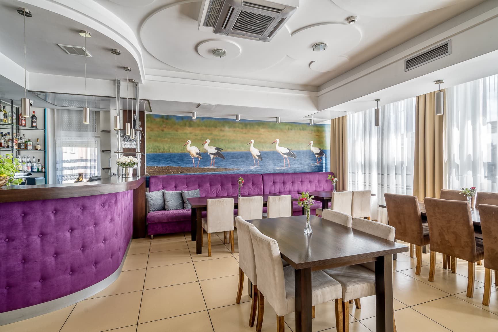 Sala restauracyjna z fioletowymi kanapami i fototapetą z bocianami